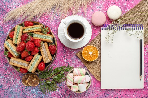 Draufsicht auf köstliche Waffelkekse mit frischen roten Erdbeeren und Macarons auf rosa Oberfläche