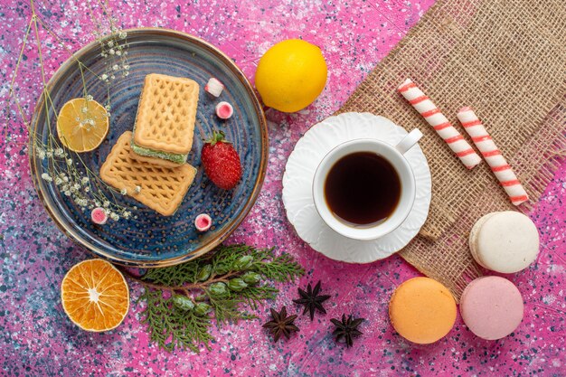 Draufsicht auf köstliche Waffeln mit französischen Macarons auf der hellrosa Oberfläche