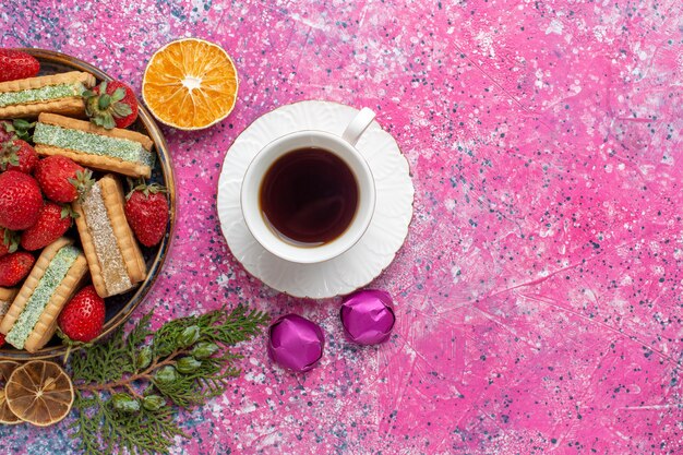 Draufsicht auf köstliche Waffeln mit Tasse Tee und frischen roten Erdbeeren auf der rosa Oberfläche