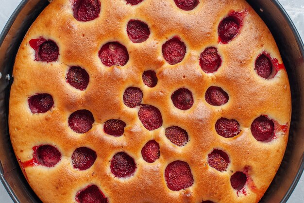 Draufsicht auf köstlichen Erdbeerkuchen, der mit frischen roten Erdbeeren innen mit Pfanne auf weißem Schreibtisch gebacken wird, Kuchenkeksfrucht süß