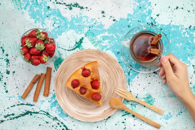 Draufsicht auf köstlichen Erdbeerkuchen geschnittenen leckeren Kuchen mit Teezimt und frischen roten Erdbeeren auf hellblauem Schreibtisch, Kuchen backen Teig süßen Zucker