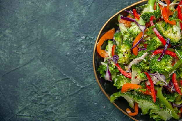 Draufsicht auf köstlichen veganen Salat in einem Teller mit verschiedenem frischem Gemüse auf der linken Seite auf dunklem Hintergrund mit freiem Platz