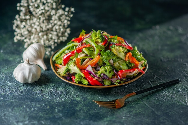 Draufsicht auf köstlichen veganen Salat mit frischen Zutaten in einer Tellergabel-Knoblauchblume auf blauem, unscharfem Hintergrund