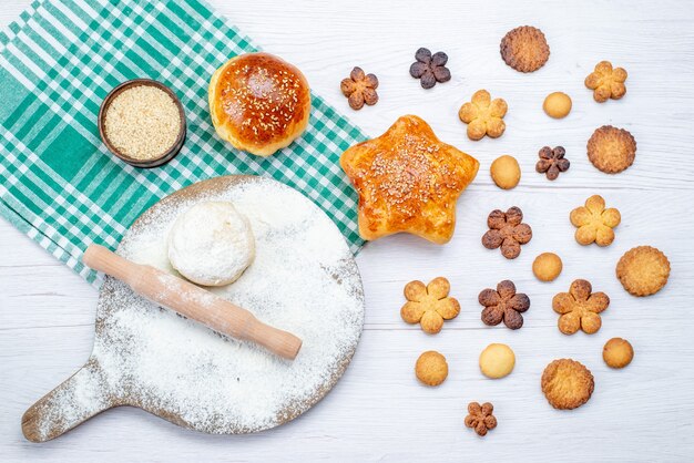 Draufsicht auf köstliches Gebäck zusammen mit Keksen und rohem Teig auf leichtem Schreibtisch, Kekskuchenkeks süßer Zucker