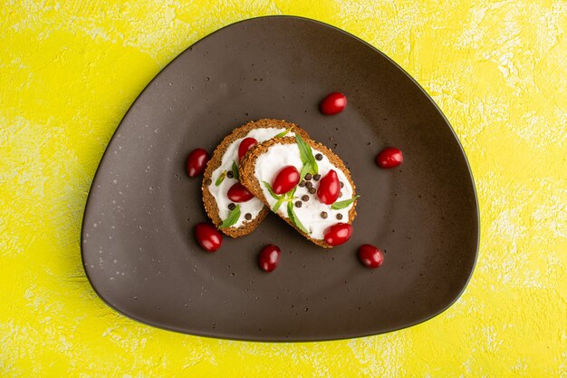 Draufsicht auf leckere Brottoasts mit saurer Sahne und Hartriegeln auf der gelben Oberfläche