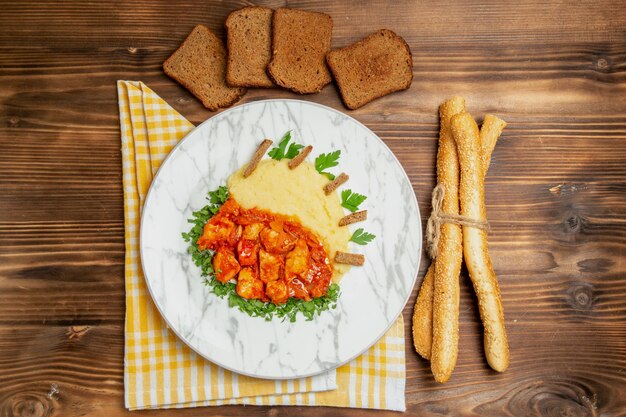 Draufsicht auf leckere Hähnchenscheiben mit Kartoffelpüree und Brot auf braunem Tisch