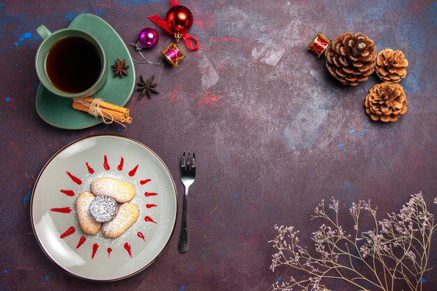 Draufsicht auf leckere Kekse mit Zuckerpulver und Tasse Tee auf Schwarz