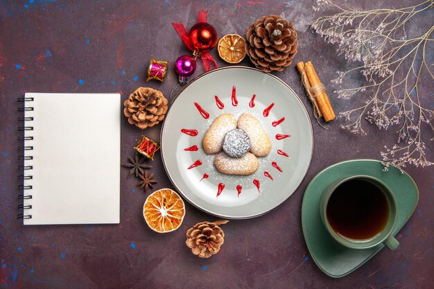 Draufsicht auf leckere Kekse mit Zuckerpulverbonbons mit einer Tasse Tee auf Schwarz on