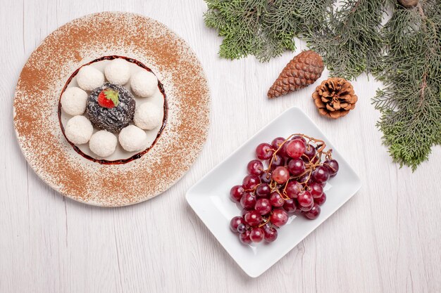 Draufsicht auf leckere Kokosbonbons mit Schokoladenkuchen und Trauben auf Weiß