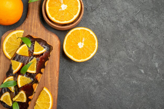 Draufsicht auf leckere Kuchen ganz und geschnittene Orangen auf Schneidebrett auf schwarzem Tisch