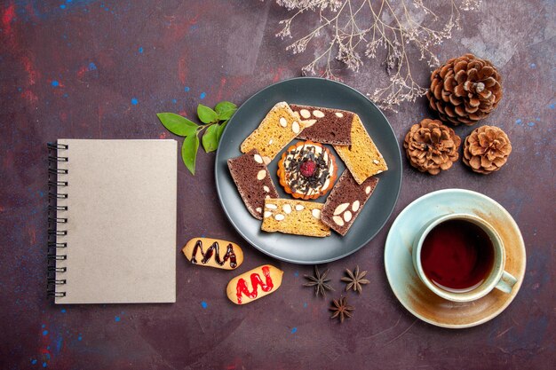 Draufsicht auf leckere Kuchenscheiben mit einer Tasse Tee auf Schwarz