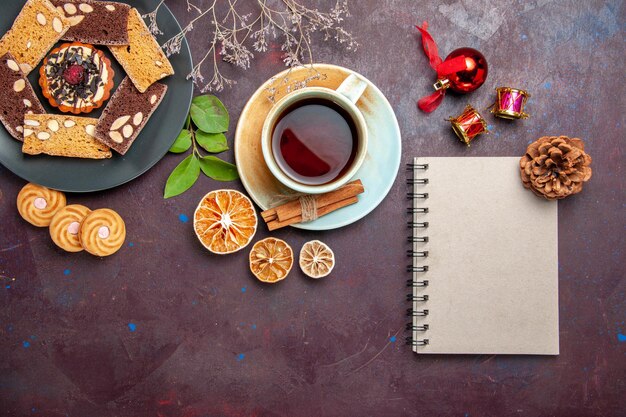 Draufsicht auf leckere Kuchenscheiben mit einer Tasse Tee auf Schwarz