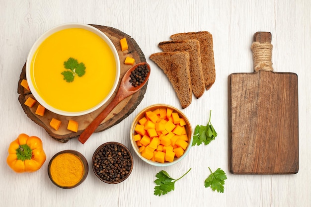 Draufsicht auf leckere Kürbissuppe mit dunklen Brotlaiben und Gewürzen auf Weiß