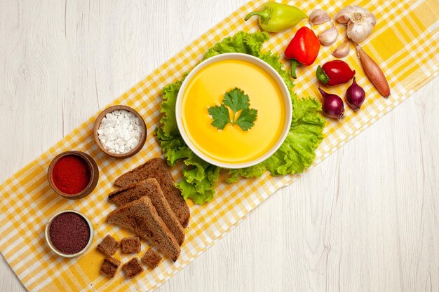 Draufsicht auf leckere Kürbissuppe mit verschiedenen Gewürzen und Brot auf Weiß