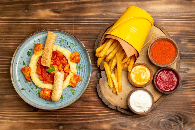 Draufsicht auf leckere Pommes Frites mit Gewürzen und Hühnchen auf braunem Tisch