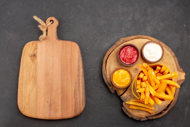 Draufsicht auf leckere Pommes Frites mit Saucen auf Schwarz