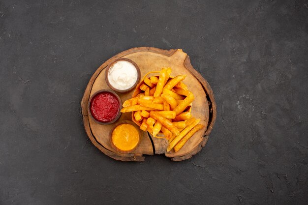 Draufsicht auf leckere Pommes Frites mit Saucen auf Schwarz