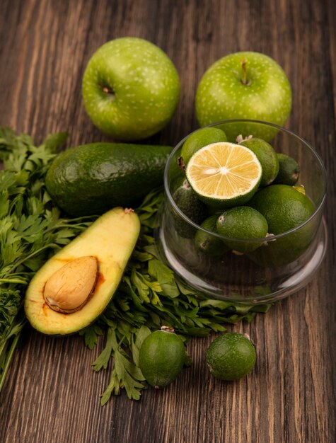 Draufsicht auf leckere reife Feijoas mit Limetten auf einer Glasschale mit Avocado-Feijoas aus grünen Äpfeln und Petersilie, isoliert auf einer Holzoberfläche