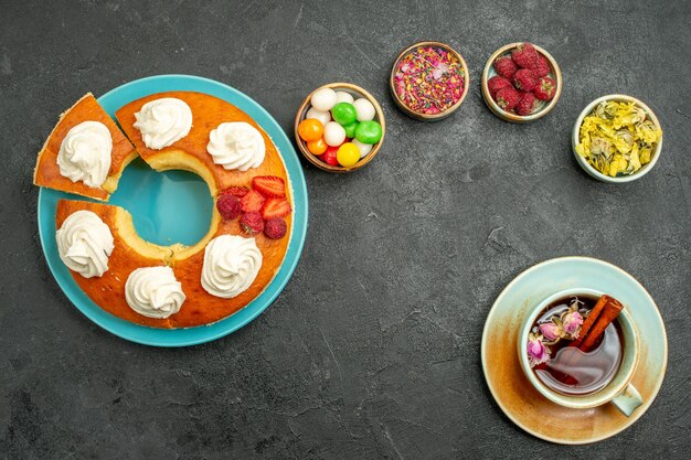 Draufsicht auf leckere Sahnetorte mit Bonbons und Tasse Tee auf Schwarz