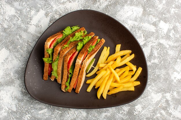 Draufsicht auf leckere Sandwiches mit grünen Salattomaten zusammen mit Pommes Frites in dunklem Teller