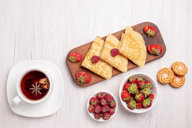 Draufsicht auf leckere süße Pfannkuchen mit Beeren und Tasse Tee auf Weiß