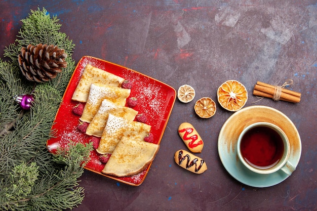 Draufsicht auf leckere süße Pfannkuchen mit Tasse Tee und Himbeeren auf Schwarz