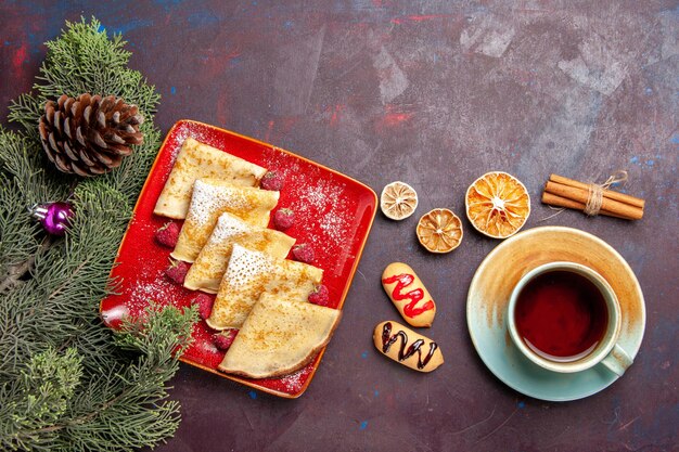 Draufsicht auf leckere süße Pfannkuchen mit Tasse Tee und Himbeeren auf Schwarz