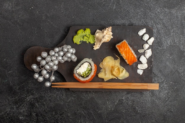 Draufsicht auf leckere Sushi-Mahlzeit geschnittene Fischröllchen mit Wassabi und Stöcken an der grauen Wand