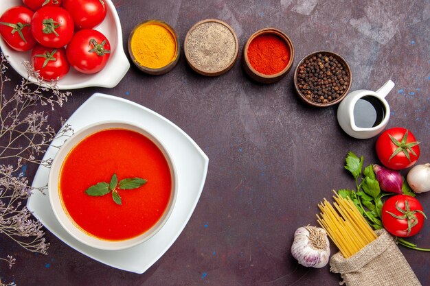 Draufsicht auf leckere Tomatensuppe mit frischen roten Tomaten und Gewürzen auf Dunkelheit