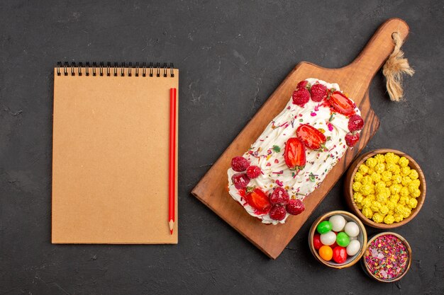 Draufsicht auf leckeren fruchtigen Kuchen mit Bonbons auf Schwarz