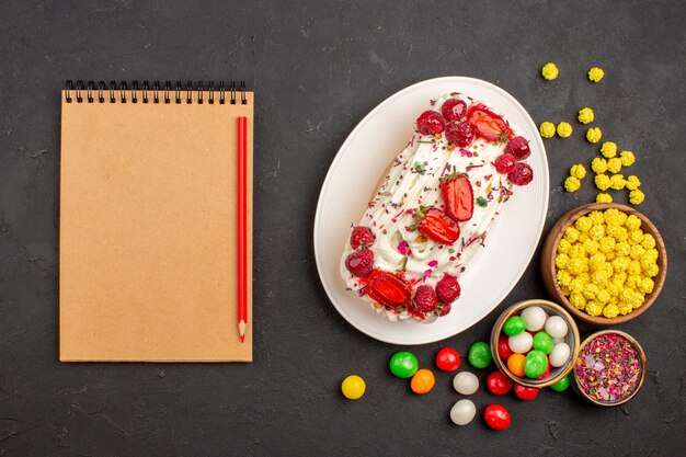 Draufsicht auf leckeren fruchtigen Kuchen mit Bonbons auf Schwarz