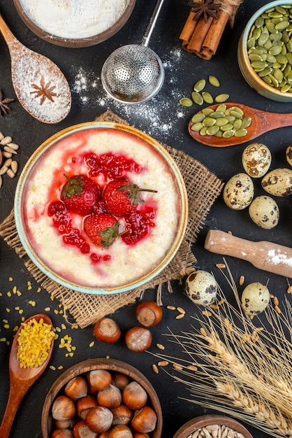 Draufsicht auf leckeres Frühstück, serviert mit Erdbeermarmelade in einer Schüssel und Honigeiermehl-Zuckerlöffeln auf dunklem Hintergrund