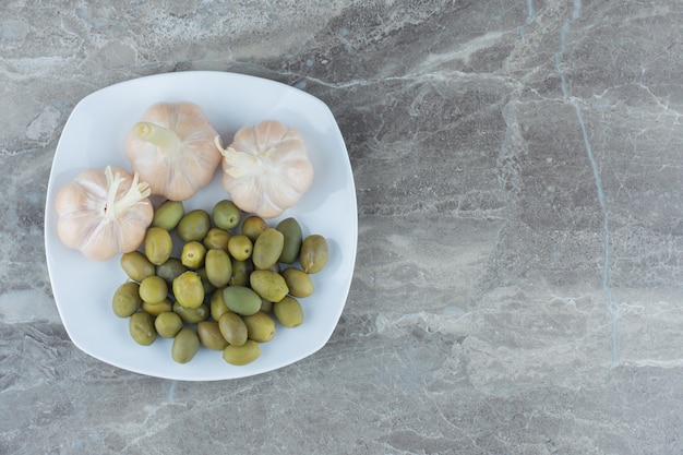 Draufsicht auf marinierte grüne Oliven und Knoblauch auf weißem Teller.