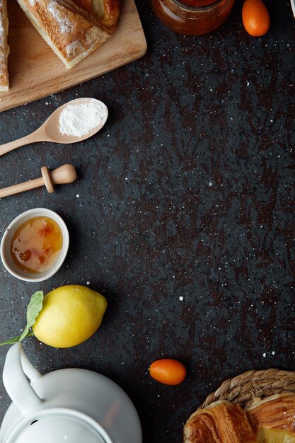 Draufsicht auf Marmeladen-Zitronen-Kumquat-Croissant-Mehl mit Teekanne auf schwarzem Hintergrund