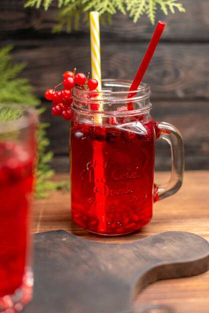 Draufsicht auf natürlichen organischen frischen Johannisbeersaft in einer Glasflasche, die mit Röhren auf einem Holzschneidebrett serviert wird