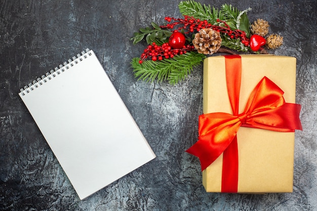 Draufsicht auf Neujahrsgeschenk mit rotem Band und Zubehördekorationen und Notizbuch auf dunkler Oberfläche