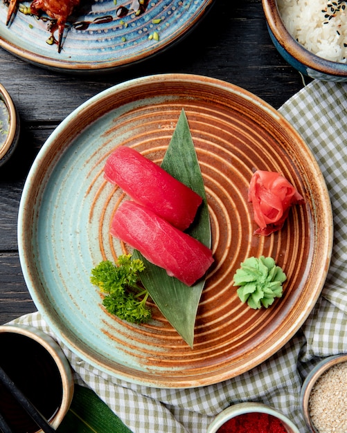 Draufsicht auf Nigiri-Sushi mit Thunfisch auf Bambusblatt, serviert mit eingelegten Ingwerscheiben und Wasabi auf einem Teller