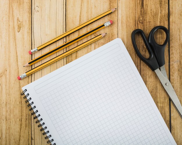 Draufsicht auf Notizblock; Schere und Stifte auf Holzbrett