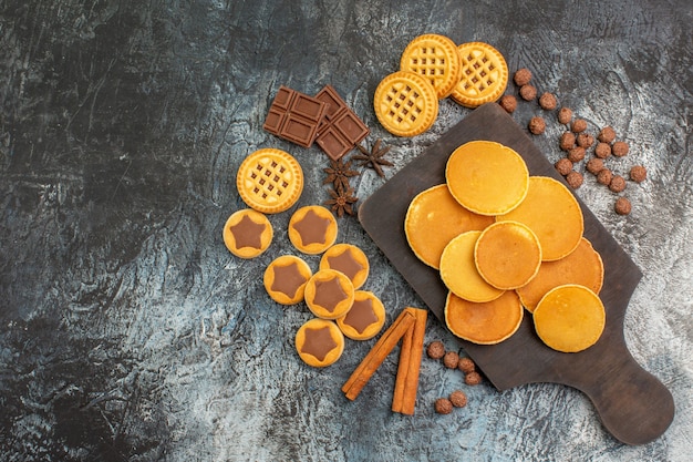 Draufsicht auf Pfannkuchen auf Holzplatte mit Keksen und Süßigkeiten auf grauem Grund