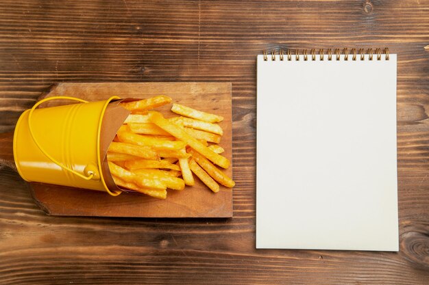 Draufsicht auf Pommes Frites im kleinen Korb mit Notizblock auf braunem Tisch