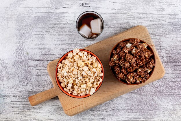 Draufsicht auf Popcorn in Schalen auf Schneidebrett und Limonade auf weißer hölzerner Horizontaler