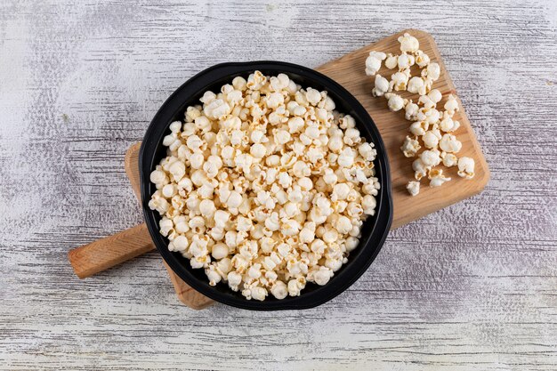 Draufsicht auf Popcorn in schwarzer Pfanne und Schneidebrett auf weißer hölzerner Horizontaler