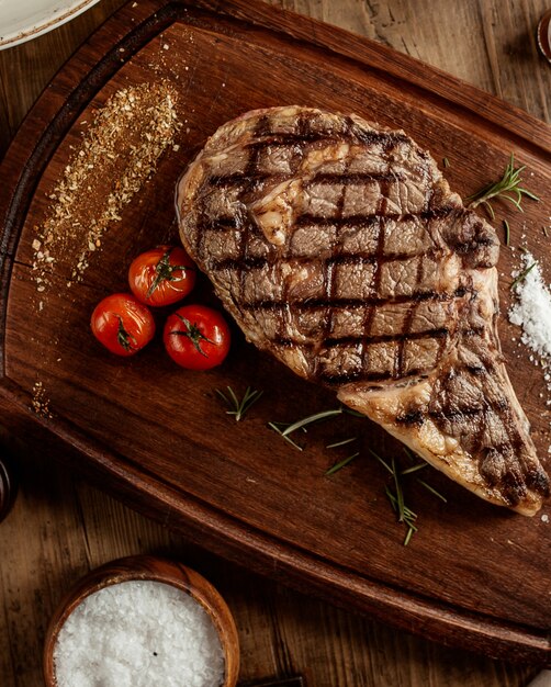 Draufsicht auf Rindersteak mit Salzkräutern und Kirschtomate an Bord serviert