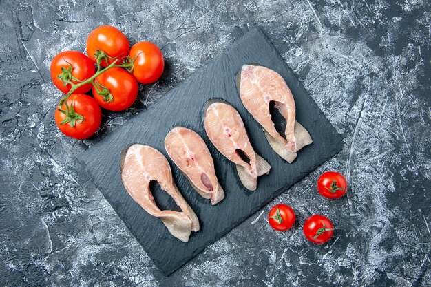 Draufsicht auf rohe Fischscheiben auf dem schwarzen Brett frische Tomaten auf dem Tisch