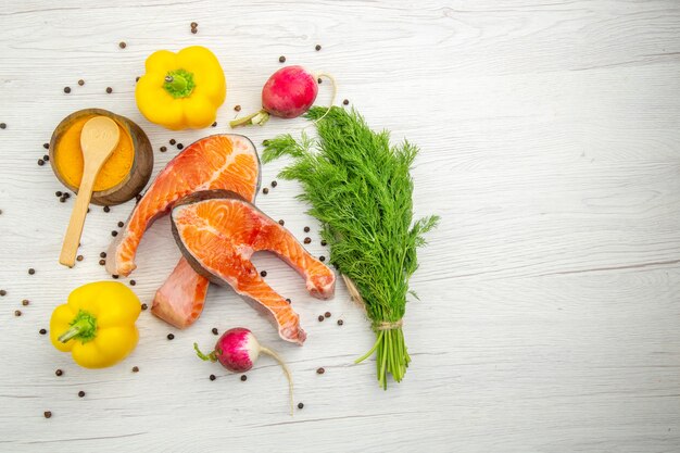 Draufsicht auf rohe Fleischscheiben mit Grüns und Paprika auf weißem Hintergrund