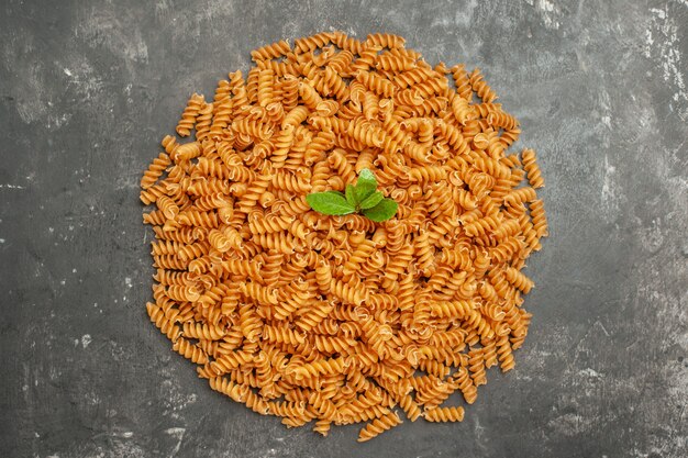 Draufsicht auf rohe italienische Pasta mit Grün im Kreis auf grauem Hintergrund angeordnet