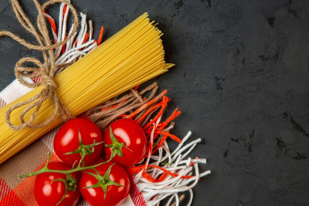 Draufsicht auf rohe Spaghetti und gebunden mit Schnur und frischen Tomaten auf Schwarz