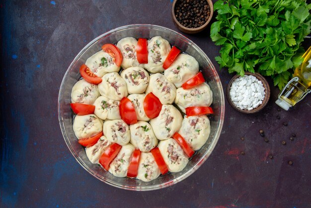 Draufsicht auf rohe Teigstücke mit Hackfleisch und frischen roten Tomaten auf einem dunklen Essensküchenfarbgerichtsfoto