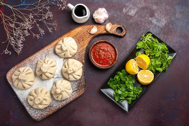 Draufsicht auf rohen Knödelteig mit Tomatensauce und Zitronenscheiben auf Schwarz