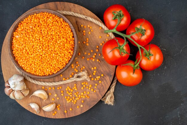 Draufsicht auf rote Linsenseilknoblauch auf hölzernen runden Bretttomaten mit Stielen auf schwarzem Hintergrund